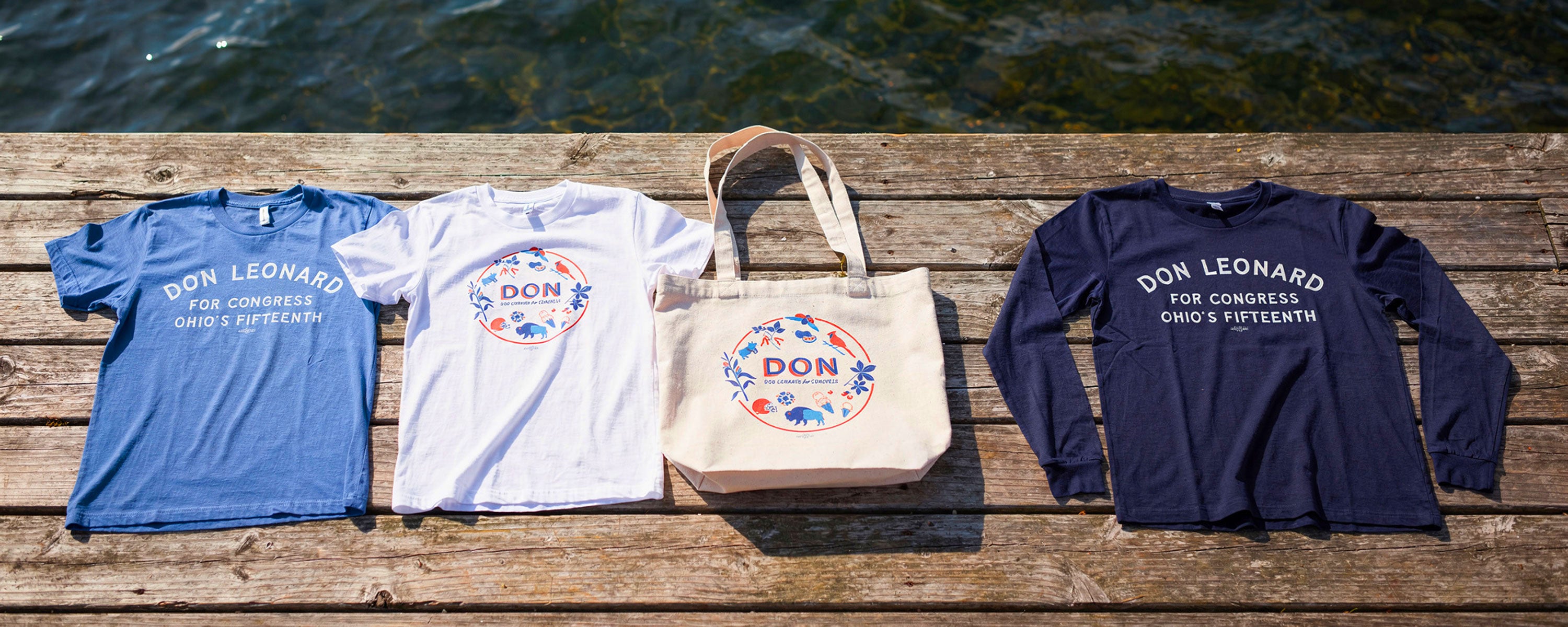 Don Leonard shirts and tote bag laid of on a dock.