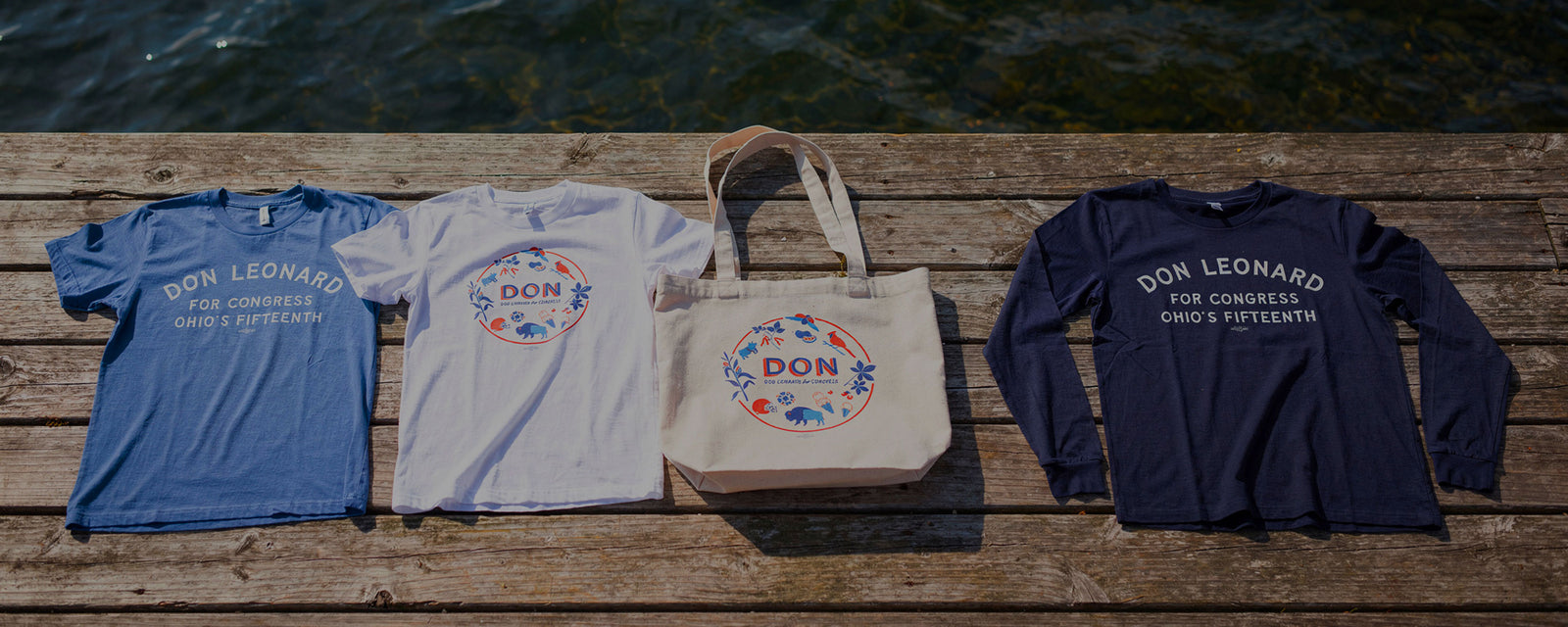 Don Leonard shirts and tote bag laid of on a dock.